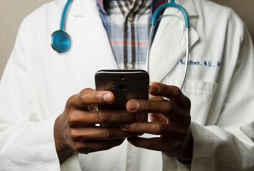 Photo of a doctor using his cellphone with a stethoscope around his neck