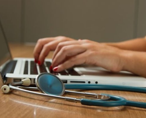 A woman typing on a laptop with a stethoscope next to it
